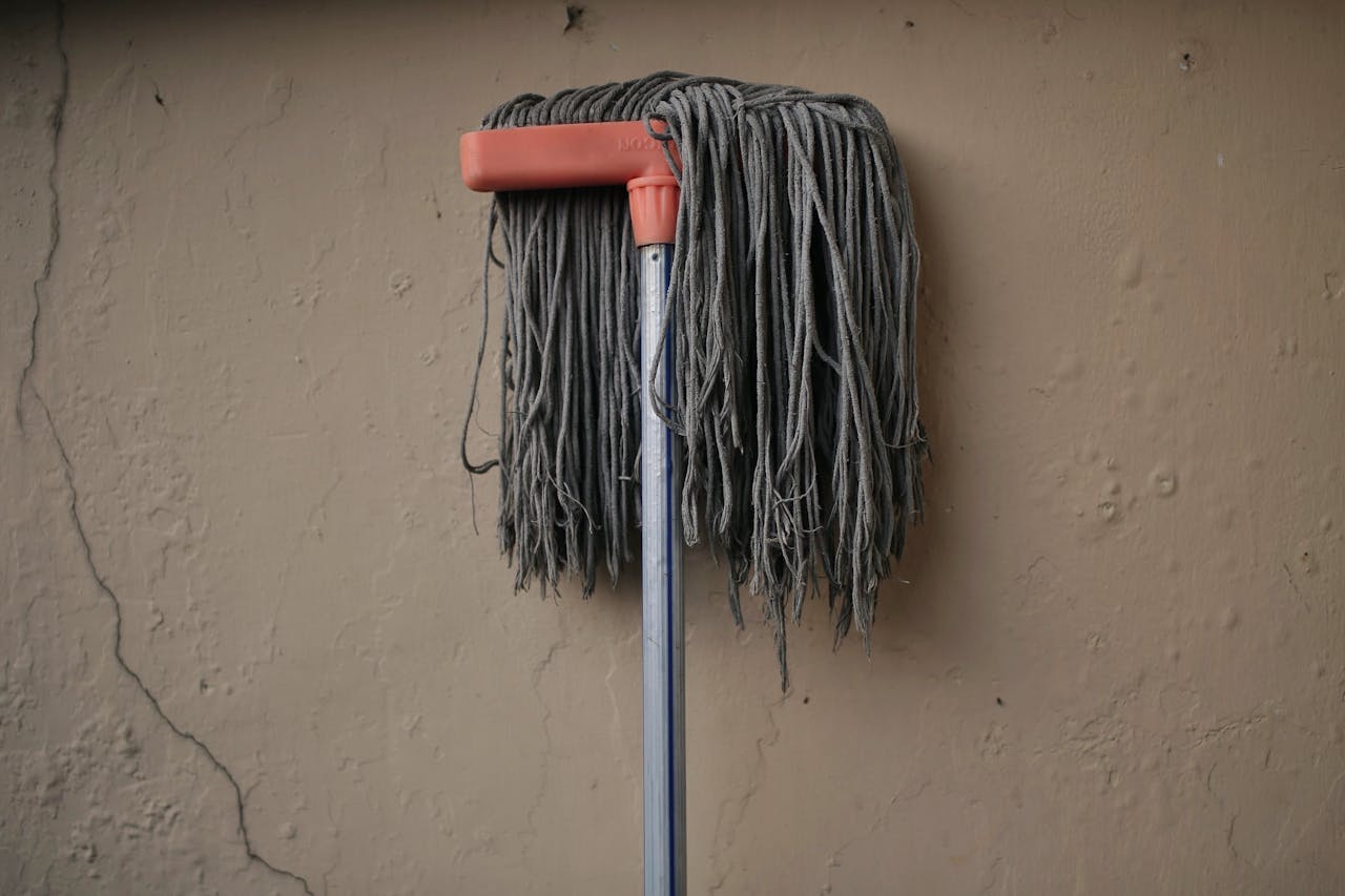 about-01 Gray mop leaning against a textured wall, conveying simplicity in a domestic setting.